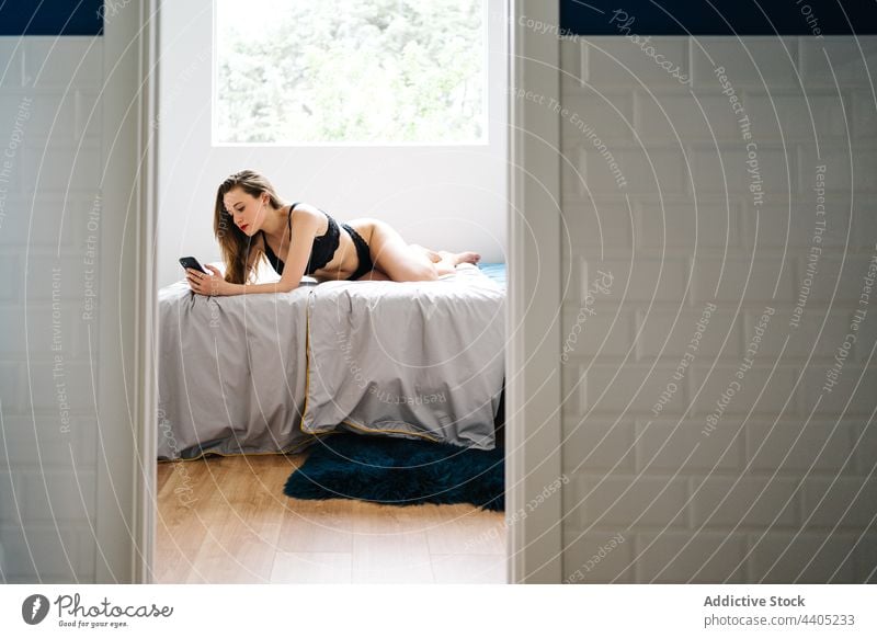 Fröhliche Frau in Unterwäsche, die im Schlafzimmer auf ihrem Smartphone surft Browsen Dessous benutzend Nachricht heiter heimwärts Mobile soziale Netzwerke