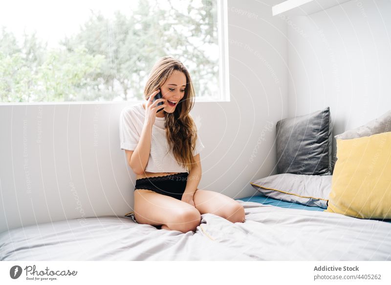 Fröhliche Frau, die auf dem Bett mit ihrem Smartphone spricht reden heimisch Frauenunterhose sprechen Gespräch Mobile Telefon Anruf jung Kommunizieren heiter