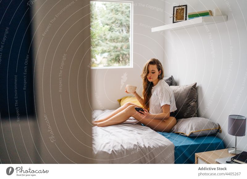 Zufriedene Frau, die morgens im Bett auf ihrem Smartphone surft Morgen benutzend Browsen Surfen trinken Tasse genießen Mobile heiter Gerät Apparatur Glück