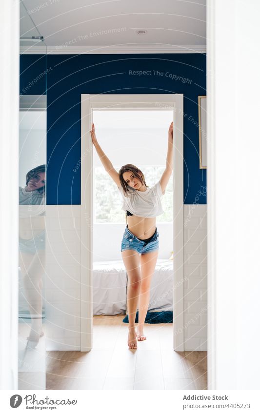 Anmutige Frau, die zu Hause in der Tür steht Türöffnung schlank verführerisch schlanke Form sinnlich Stil heimwärts Jeansstoff Shorts T-Shirt trendy Verlockung