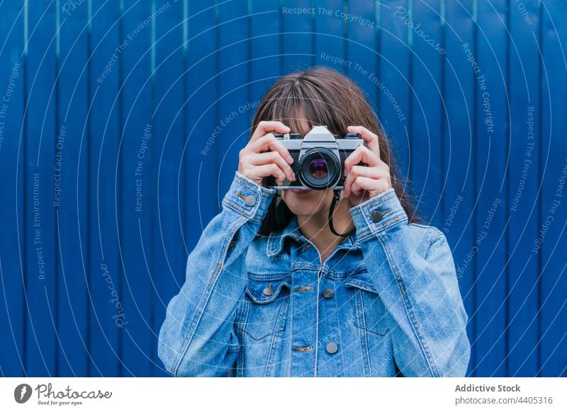 Unbekannte Frau fotografiert mit Retro-Kamera vor blauer Wand Fotograf Fotoapparat fotografieren retro altehrwürdig Farbe Gedächtnis Moment Hobby Fotografie
