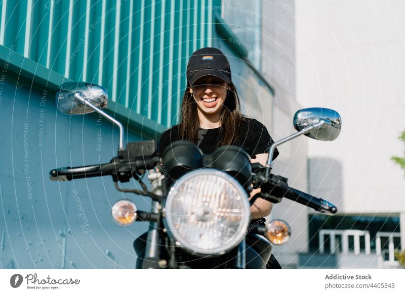 Fröhliche Frau sitzt auf einem Motorrad und schaut in die Kamera Biker Motorradfahrer heiter geparkt Großstadt Lächeln Reiter Verkehr Fahrzeug urban sitzen