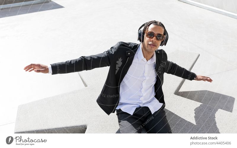 Glücklicher Geschäftsmann mit Kopfhörern und Sonnenbrille auf der Straße Stil trendy Musik genießen urban sorgenfrei jung Mann ethnisch Geflecht Afroamerikaner