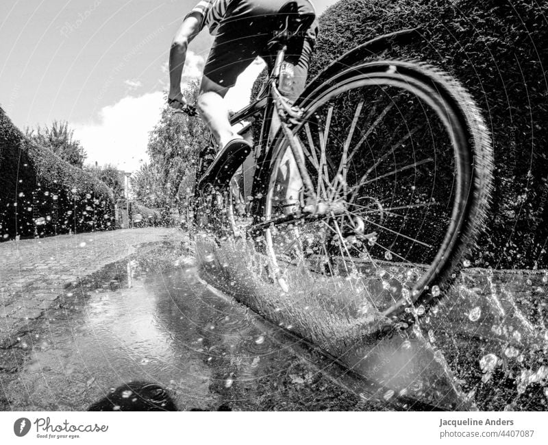 Radfahrer fährt durch eine Pfütze Aktivität Unschärfe Sommer Freizeit & Hobby grau Wege & Pfade Wetter Außenaufnahme Menschen Transport Gesundheit Spaß haben