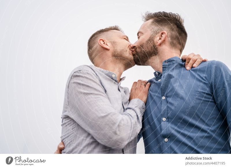 Fröhliches schwules Paar, das sich unter hellem Himmel küsst lgbt Lachen Kuss interagieren Zeit verbringen Partnerschaft romantisch offen Männer