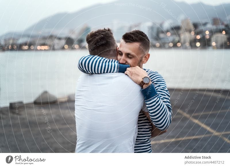 Homosexuelles Paar umarmt sich auf dem Bürgersteig am Stadtfluss Umarmen Liebe Partnerschaft romantisch lgbt herzlich genießen Großstadt Männer Straßenbelag See
