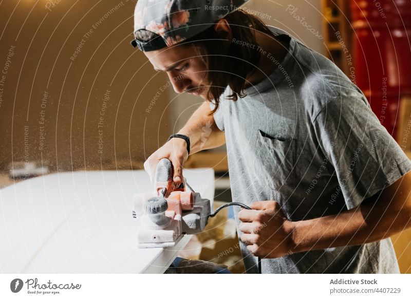 Surfboard-Shaper mit elektrischer Hobelmaschine in der Werkstatt Surfbrett Form Formgeber Werkzeug polnisch Oberfläche Mann männlich professionell Gerät behüten