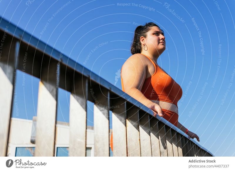Ethnische Sportlerin mit Übergewicht hinter einem Zaun im Sonnenlicht Blauer Himmel beschaulich Körper Pause bewundern angenehm allein Frau Athlet mollig