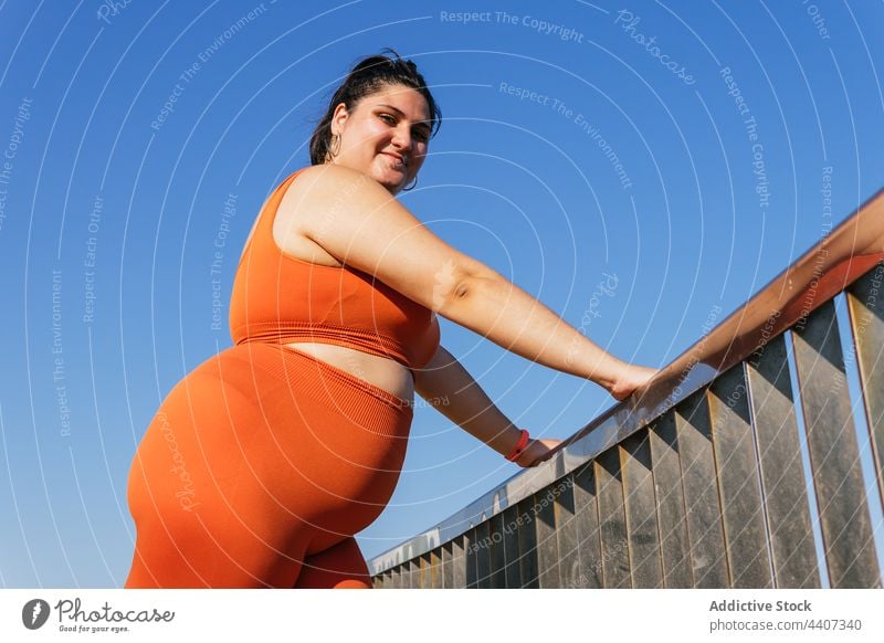 Ethnische Sportlerin mit Übergewicht lehnt sich an den Zaun im Sonnenlicht Blauer Himmel beschaulich Körper Pause bewundern angenehm allein Frau Athlet mollig