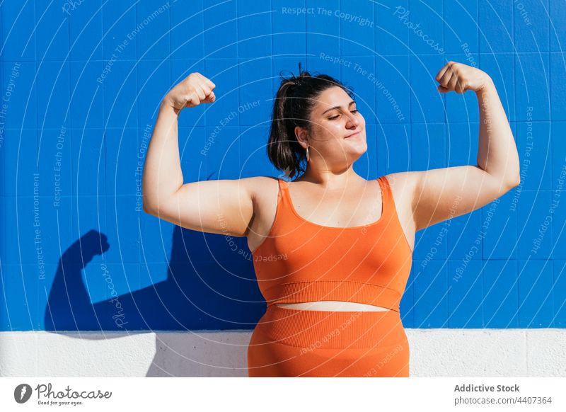 Starke übergewichtige ethnische Sportlerin zeigt Bizeps im Sonnenlicht stark Kraft selbstbewusst Training Übergröße Straße Frau selbstsicher zeigen
