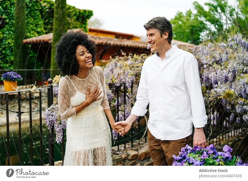 Positives multiethnisches Paar hält sich im Park mit Blumen an den Händen Garten Spaziergang Händchenhalten Blütezeit heiter Zusammensein Partnerschaft