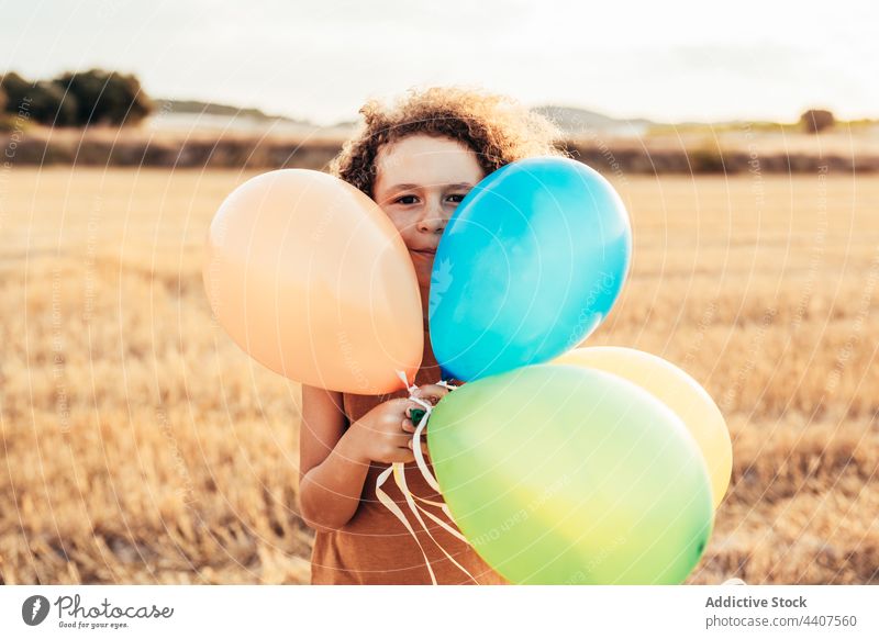 Unbekümmertes ethnisches Kind spielt mit bunten Luftballons im Feld spielen Wind spielerisch sorgenfrei Freiheit Sommer Lächeln heiter Kindheit Glück niedlich
