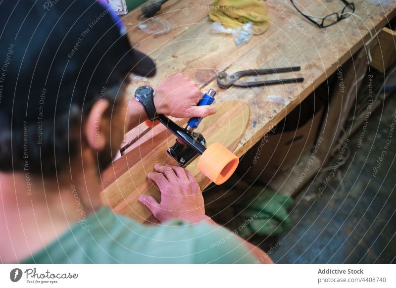 Fokussierter Handwerker, der in einer leichten Werkstatt ein Skateboard herstellt Kunstgewerbler Rad befestigen professionell handgefertigt Talent Mann machen