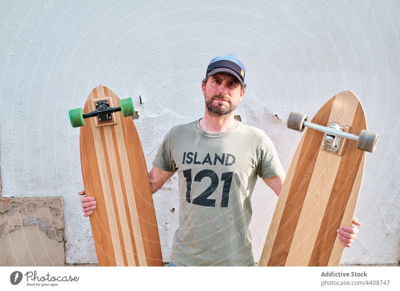 Skater mit Longboards auf dem Bürgersteig im Sonnenlicht handgefertigt kreativ Design Stil Sport modern Mann Straßenbelag Jeanshose Wand Skateboard nachdenken
