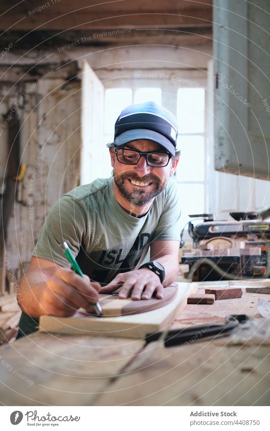 Lächelnder Handwerker mit Marker und Holzklötzen auf einer Werkbank Kunsthandwerker Spur Markierung Skateboard Herstellung Schiffsplanken Holzarbeiten
