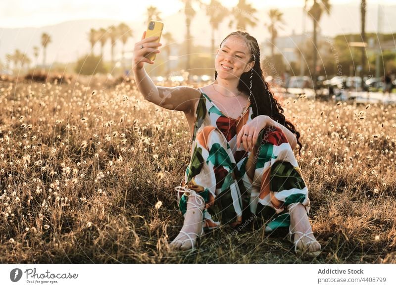 Entzückte Frau mit Vitiligo, die ein Selbstporträt mit dem Smartphone auf einer Wiese aufnimmt Selfie Browsen Feld Sommer Sonnenuntergang Hauterkrankung