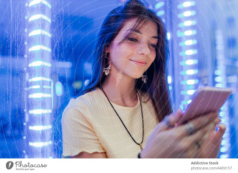 Lächelnde Frau, die in Neonlichtern mit ihrem Smartphone chattet plaudernd neonfarbig interessiert Internet online freie Zeit Stadt benutzend Apparatur Gerät