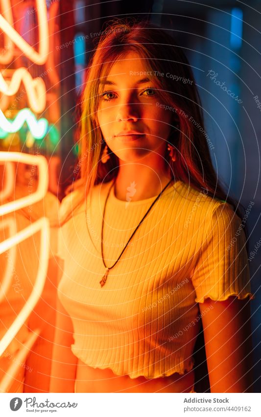 Zärtliche Frau beleuchtet auf Neonlicht Wand in der Nacht neonfarbig orange Glaswand herzlich sanft sensibel allein Starrer Blick Porträt Licht Abenddämmerung