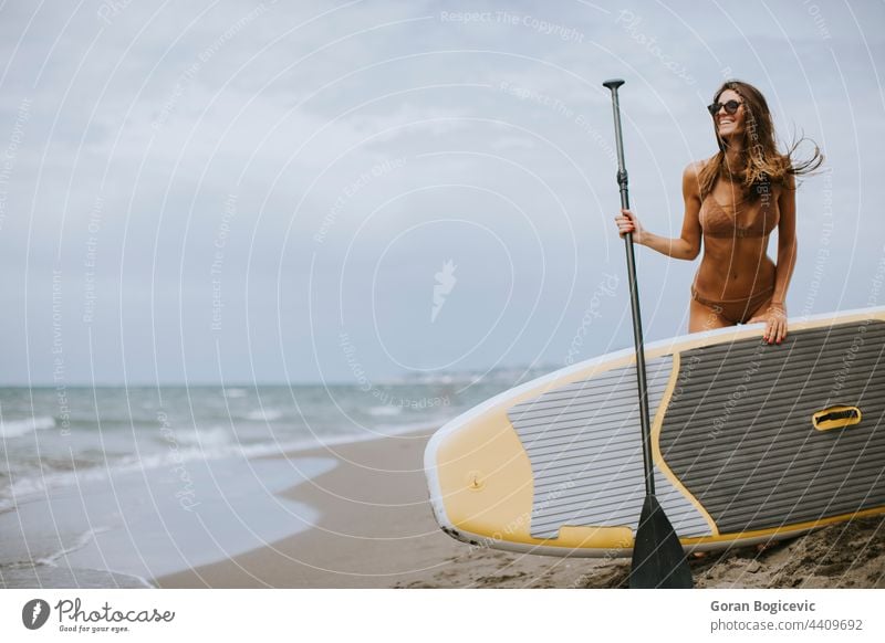Junge Frauen mit Paddelbrett am Strand an einem Sommertag attraktiv schön Bikini Holzplatte Küste Tag passen Spaß Glück Beteiligung Lifestyle Meer im Freien