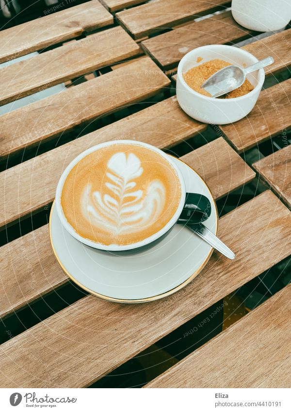 Cappuccino mit Latte Art auf einem Holztisch in einem Café Kaffee Gastronomie Heißgetränk Barista Tasse brauner Zucker Frühstück Kaffeetrinken