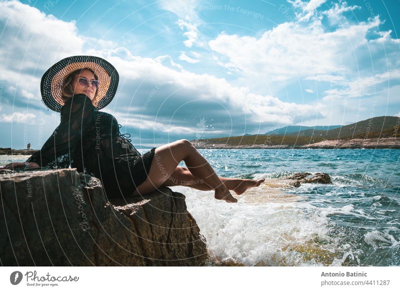 Erstaunlich Blick auf eine Brünette sitzt auf einem Felsen in der Nähe des Meeres. Erstaunliche Sommerwetter in Kroatien, vis Insel. Sonnenbaden in der Sonne mit Wellen, die an das Ufer schlagen