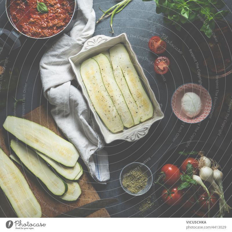 Kochen von Zucchini-Lasagne. Auflauf mit geschnittenen Zucchini und fertiger Bolognesesauce auf dem Küchentisch mit frischen Zutaten: Tomaten, Mozzarella und Kräutersalz. Ansicht von oben
