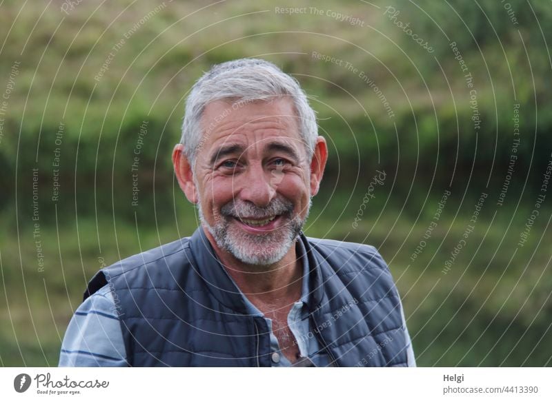Porträt eines lachenden Senioren mit kurzen grauen Haaren und grauem Bart Mensch Mann Lachen Freundlichkeit grauhaarig kurze Haare Weste T-Shirt draußen
