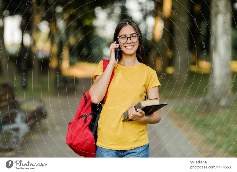 Porträt einer schönen Brünetten mit Brille und einem Rucksack, die im Park telefoniert Mädchen Schüler Telefon sprechend laufen Campus hübsch Bücher Lächeln