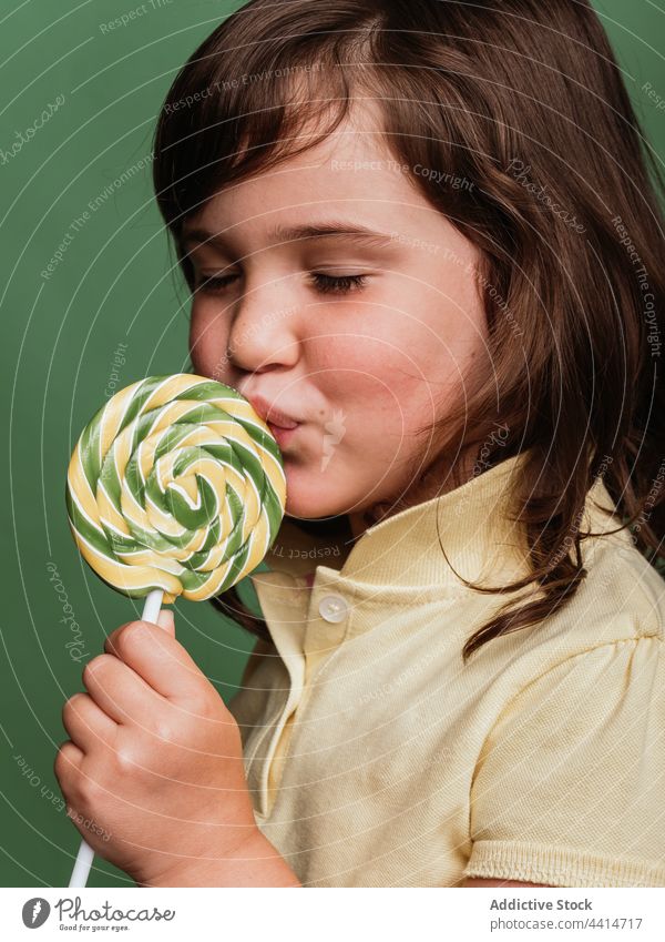 Fröhliches Mädchen mit Spirale Süßigkeiten auf grünem Hintergrund lutschen Lollipop Verwirbelung Bonbon süß lustig Kind Dessert niedlich bezaubernd Glück