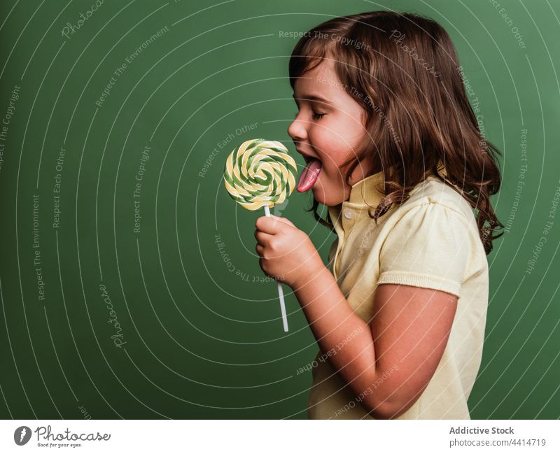Fröhliches Mädchen mit Spirale Süßigkeiten auf grünem Hintergrund lutschen Lollipop Verwirbelung Bonbon süß lustig ausspannen Kind Dessert niedlich bezaubernd