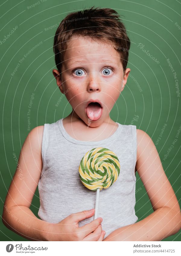 Fröhliches Kind mit Lutscher am Stiel auf grünem Hintergrund Lollipop ausspannen kleben Verwirbelung Daumen hoch mögen gestikulieren Zeichen heiter Junge Glück