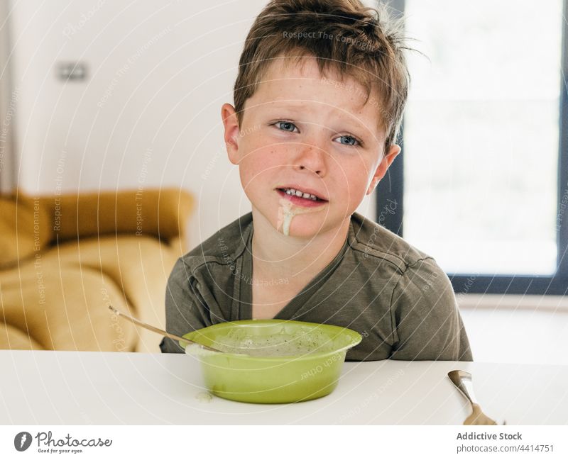 Trauriges Kind mit schmutzigem Mund beim Mittagessen zu Hause dreckig angewidert traurig Lebensmittel Junge Mahlzeit Schalen & Schüsseln Tisch sitzen Kindheit
