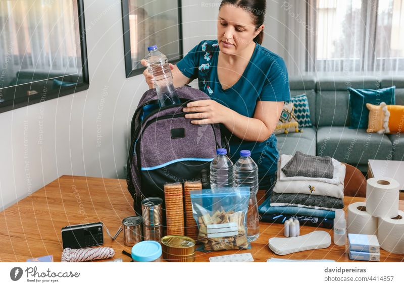 Frau setzt eine Wasserflasche ein, um einen Notfallrucksack vorzubereiten Setzen Wasserflaschen vorbereitend Rucksack Notfalltasche 72 Stunde Notfallevakuierung