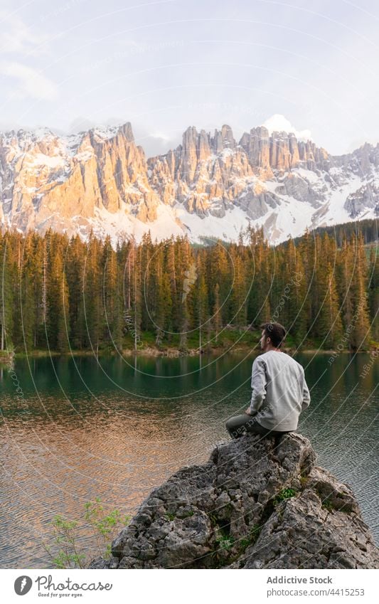 Reisender Mann sitzt auf einem Felsen in der Nähe eines Teiches in den Bergen See Berge u. Gebirge bewundern reisen Hochland Sonnenuntergang Entdecker männlich