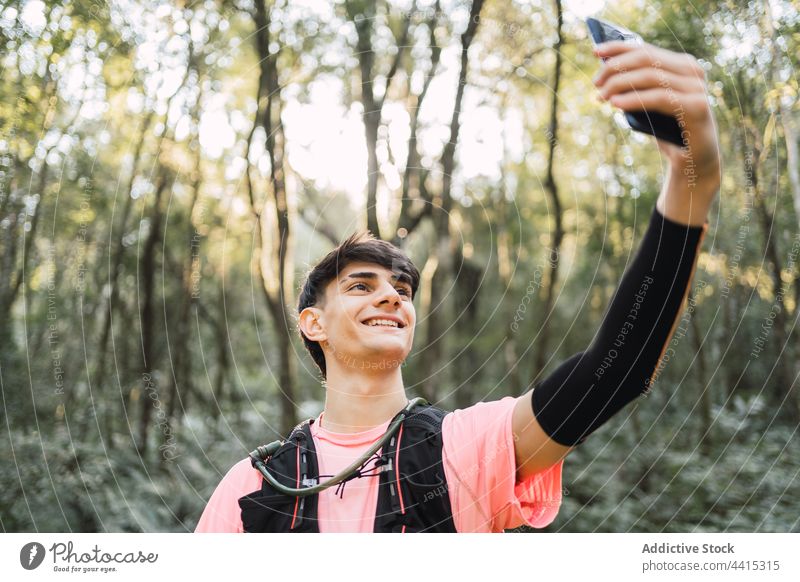 Lächelnder Reisender, der während einer Wanderung ein Selfie mit seinem Smartphone macht Mann Browsen Rucksack Trekking Wald benutzend Wanderer reisen männlich