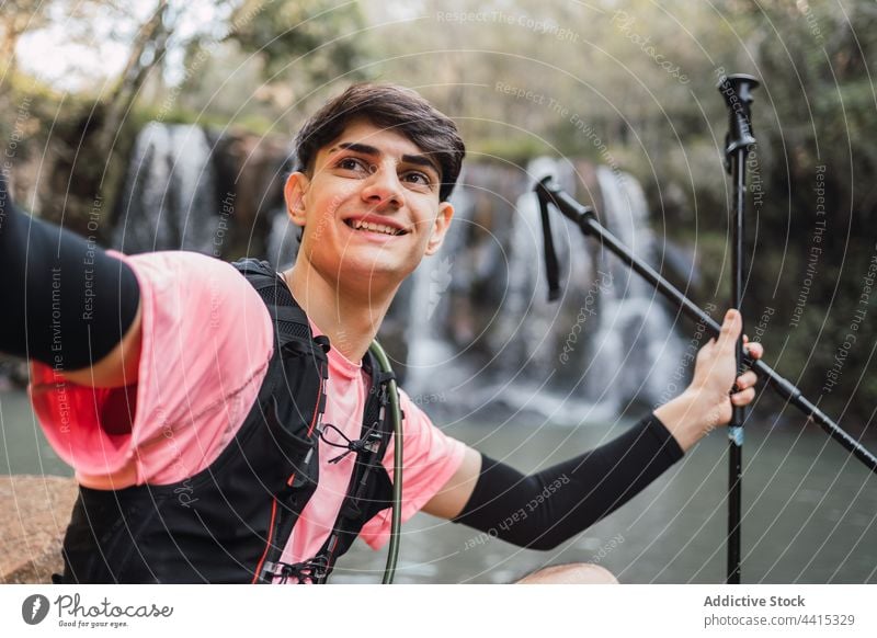 Reisender Mann nimmt Selfie gegen Wasserfall im Wald Smartphone Selbstportrait Wanderer Trekking Gedächtnis männlich Natur heiter benutzend fotografieren reisen