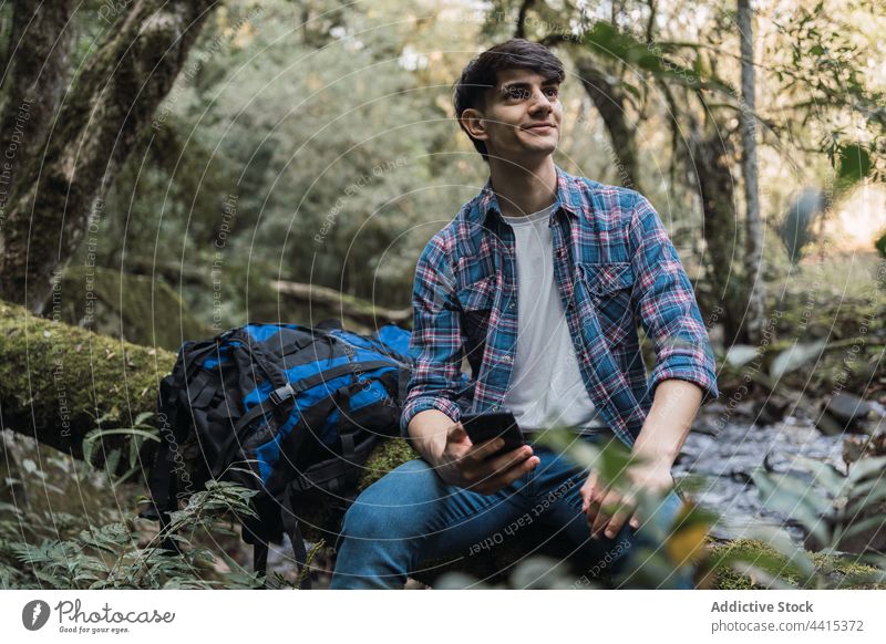 Lächelnder Reisender mit Smartphone während einer Wanderung Mann Browsen Rucksack Trekking Wald benutzend Wanderer reisen männlich Natur Apparatur Inhalt Gerät