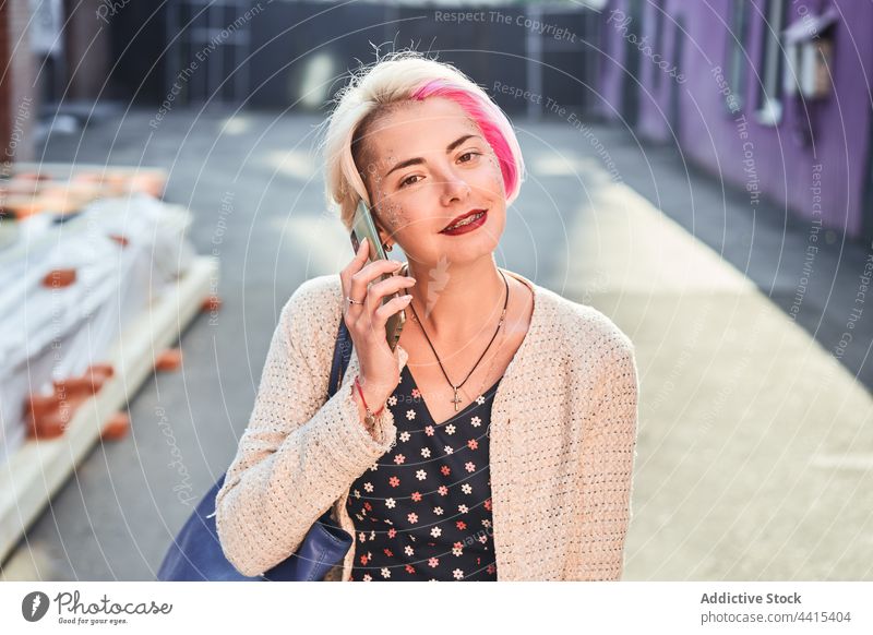Lächelnde, informelle Frau, die in der Stadt mit ihrem Smartphone spricht alternativ sprechen reden Großstadt Subkultur Gespräch Mobile heiter Anruf Apparatur