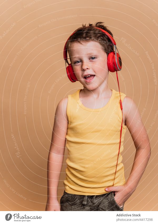 Fröhliches Kind, das mit Kopfhörern Musik hört und singt zuhören singen Gesang genießen Junge unterhalten Atelier Gerät Apparatur Klang Stil cool Vergnügen