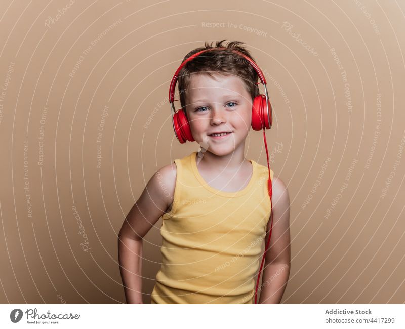 Fröhliches Kind, das mit Kopfhörern Musik hört zuhören Gesang genießen Junge unterhalten Atelier Gerät Apparatur Klang Stil cool Vergnügen Talent Audio Kindheit
