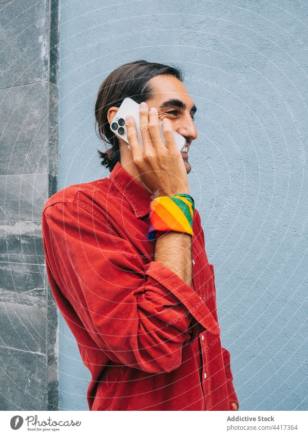 Fröhlicher ethnischer homosexueller Mann, der mit einem Smartphone spricht schwul reden Homosexualität Großstadt Straße Telefonanruf lgbt Regenbogen männlich