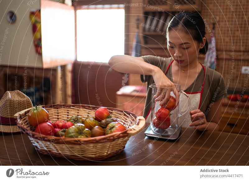 Asiatische Frau wiegt Tomaten auf einer Küchenwaage Skala wiegen Koch Hausfrau Lebensmittel vorbereiten Gemüse ethnisch asiatisch heimwärts Glas Kannen Krug