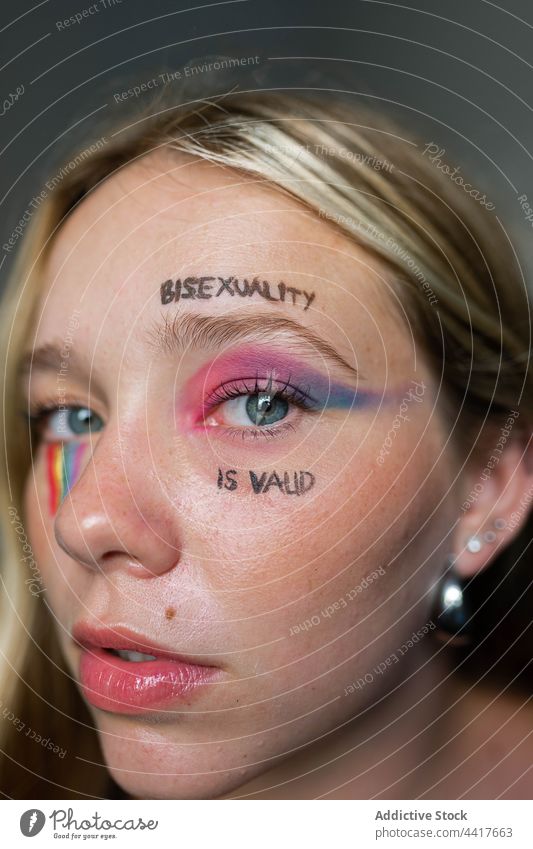 Junge lesbische Frau mit hellem Make-up schaut in die Kamera lgbtq Homosexualität bisexuell Stolz Fahne Regenbogen Toleranz Aufschrift Bisexualität ist gültig