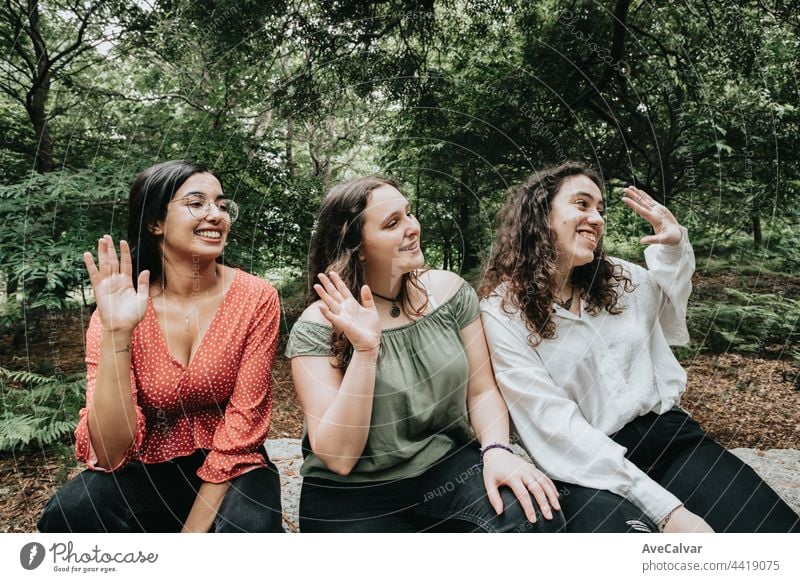 Drei junge Frauen grüßen jemanden aus dem Off im Wald, multikulturelles Freundschaftskonzept, Glückskonzept Schüler Teenager in die Kamera schauen Gruß Lächeln