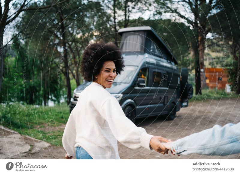 Multiethnisches Paar hält sich an den Händen, während es gegen einen Wohnwagen im Lager läuft Händchenhalten Spaziergang Wohnmobil Lächeln Zeit verbringen