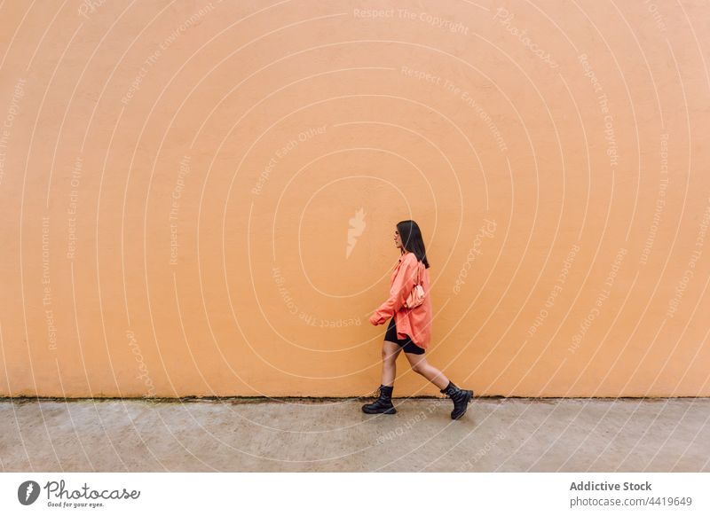 Junge Frau geht in der Nähe der orangefarbenen Wand cool Stil modern Straße trendy tausendjährig Individualität selbstbewusst Vorschein Sonnenbrille schlendern