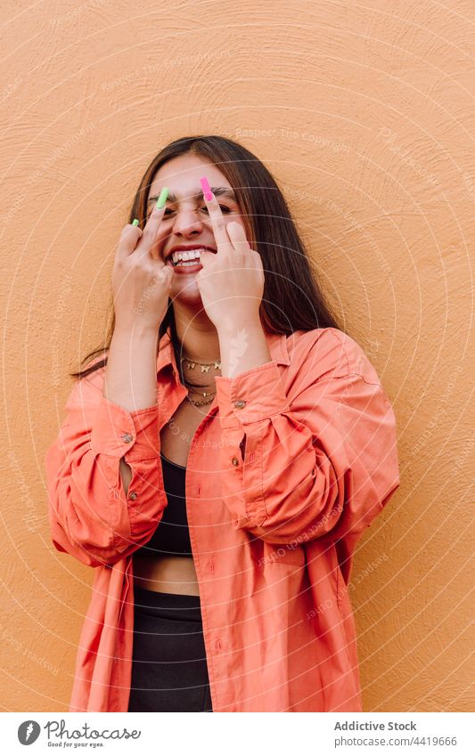 Ausdrucksstarke Frau zeigt Fickgesten gegen orangefarbene Wand ficken gestikulieren unanständig provokant Verhalten Lachen zeigen cool expressiv spielerisch