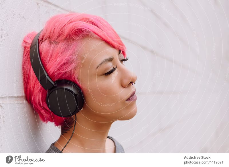 Junge Frau mit Kopfhörern und geschlossenen Augen Musik modern gefärbtes Haar Straße hell Gerät urban Audio Frisur jung verträumt Vorschein Individualität