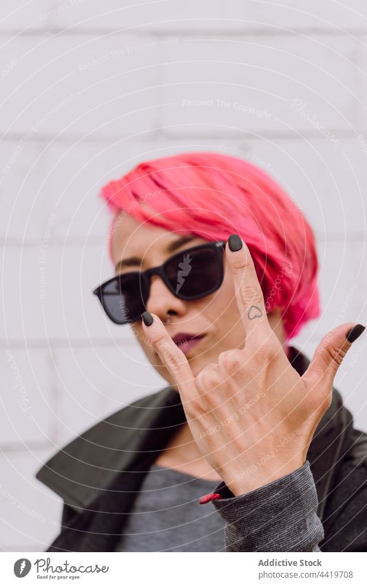 Frau mit rosa Haaren, die Anzeichen von Hörnern zeigen gestikulieren Sonnenbrille Hupe Stil modern Rock and Roll brutal auflehnen hell Hipster Zeichen