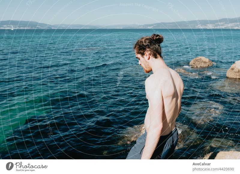 Junger Mann schaut auf das Meer, bevor er ins Wasser springt, Mittelmeerurlaub, Freiheit und Freiheitsbegriffe, moderner, blasser Mann horizontal Stehen Tourist